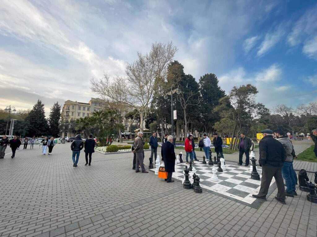 men watching a chess match on a life-size board near the waterfront in Baku