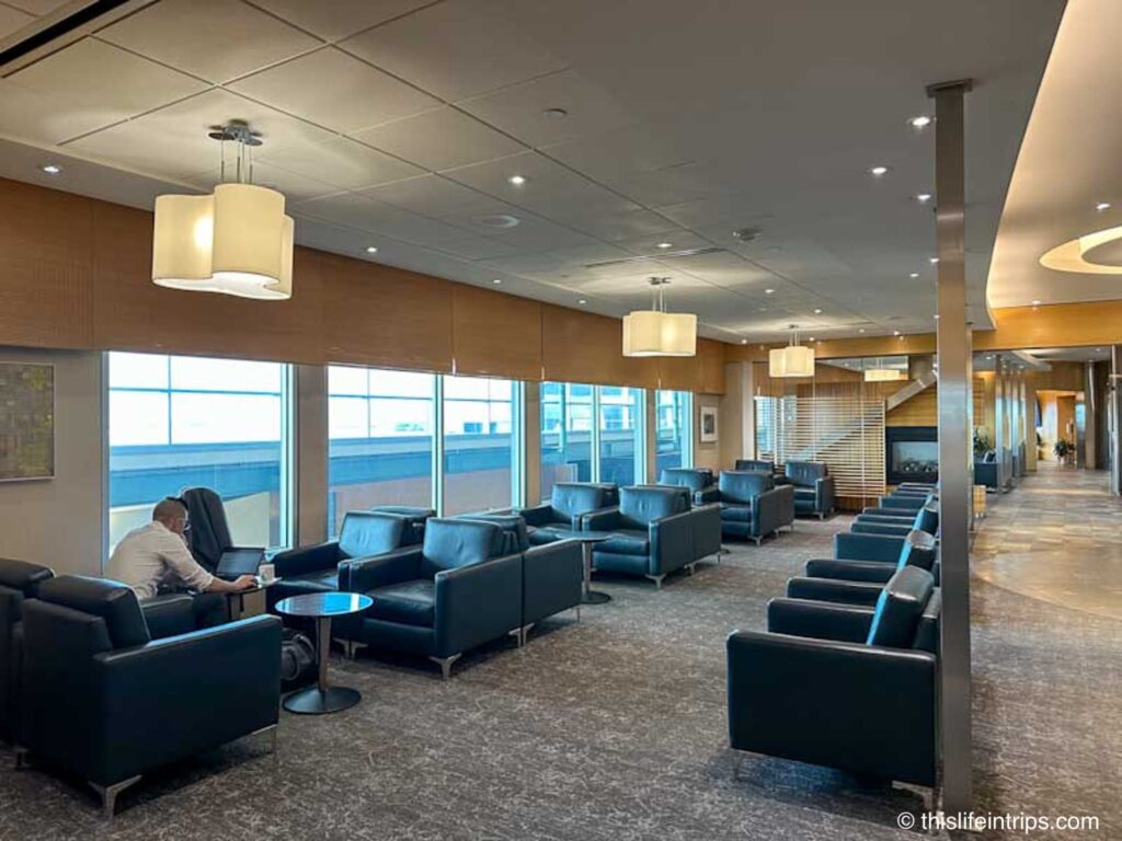 Edmonton Plaza Premium lounge leather seats and small tables in a row along a window. One man is working on the closest table.