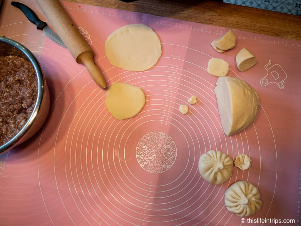 top down shot of two balls of dough and rolled out dough next to large bowl of meat mixture for khinkali