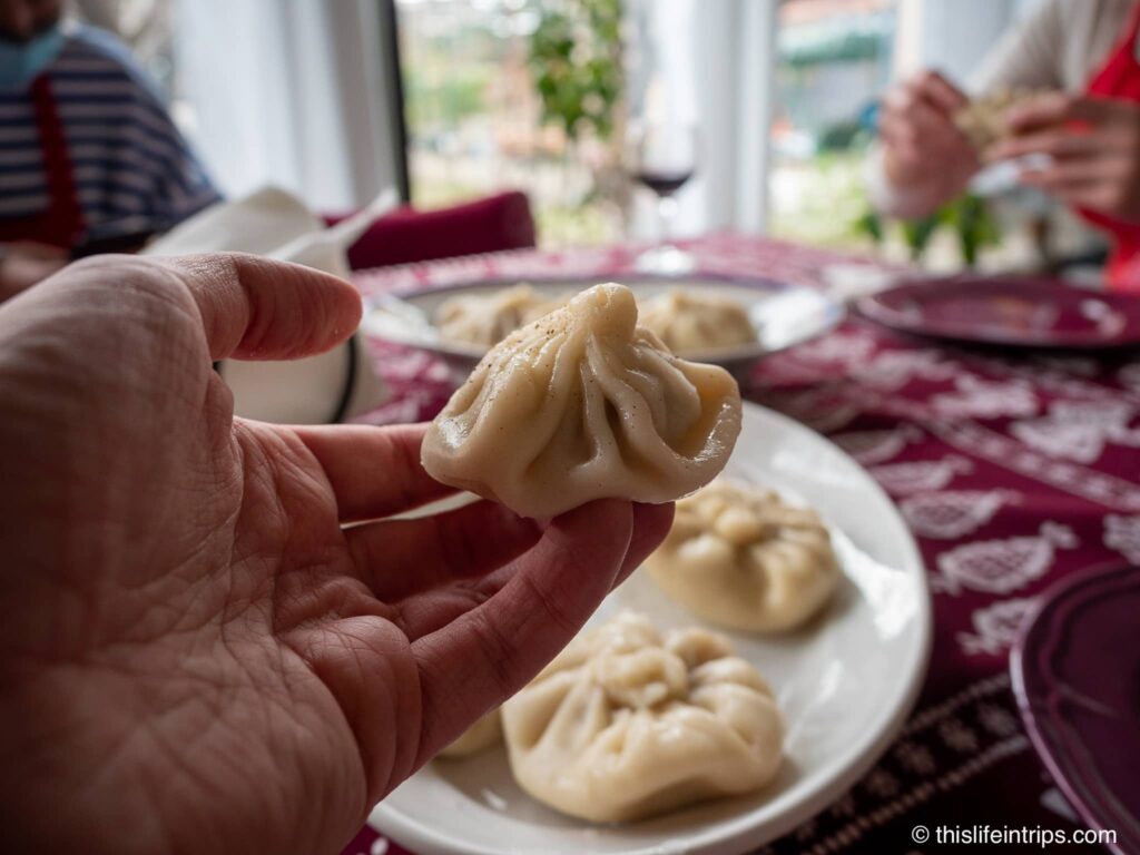 hand holding up a khinkali in front of plate