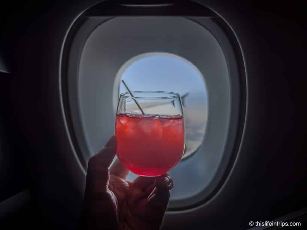 A hand holding a A Singapore Sling in front of a airplane window