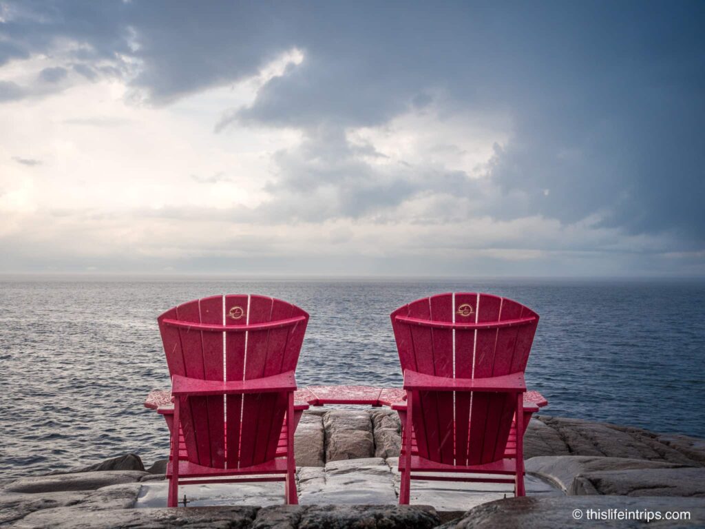 Red Parks Canada chairs on rocky shore of Cap-de-Bon-Désir Interpretation and Observation Centre
